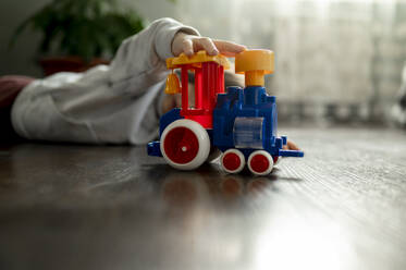 Junge liegt auf dem Boden und spielt mit Spielzeugeisenbahn - ANAF00495