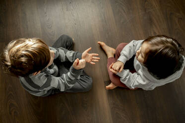 Junge mit Bruder spielt Stein-Papier-Schere auf dem Boden zu Hause - ANAF00497