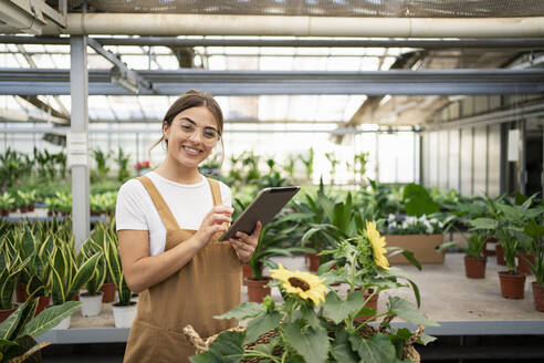 Happy gardener with tablet PC standing in plant nursery - RCPF01481