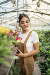 Gardener with eyes closed leaning on rack in greenhouse - RCPF01486