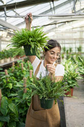 Glückliche junge Gärtnerin mit Pflanzen in der Gärtnerei - RCPF01490