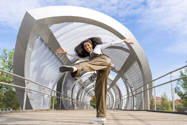 Lächelnde junge Frau tanzt auf einer Brücke - DLTSF03422
