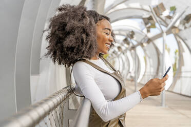 Young woman using mobile phone leaning on railing - DLTSF03433