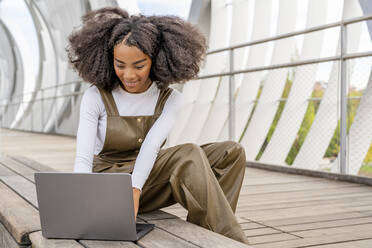 Woman using laptop sitting on footbridge - DLTSF03442