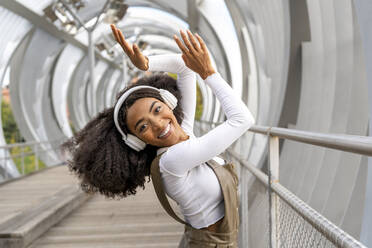 Glückliche Frau, die auf einer Fußgängerbrücke über Kopfhörer Musik hört - DLTSF03445