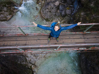 Austria, Lower Austria, Annaberg, Drone view of female hiker standing with raised arms on bridge stretching over Otscherbach river - HMEF01432