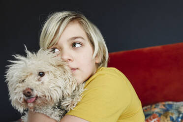 Boy with blond hair embracing dog at home - EYAF02323
