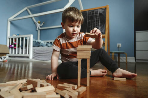 Boy playing with wooden block in bedroom at home - EYAF02340