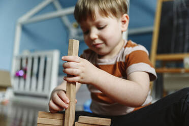 Lächelnder Junge spielt mit Holzklotz im Schlafzimmer zu Hause - EYAF02341