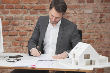 Architekt prüft Papierkram am Schreibtisch sitzend am Arbeitsplatz - DHEF00666