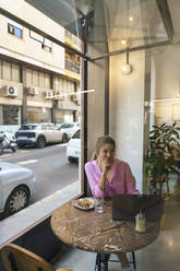 Lächelnder junger Freiberufler sitzt mit Laptop am Tisch im Café - JOSEF14725