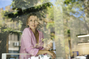 Happy young businesswoman with smart phone seen through glass at cafe - JOSEF14739