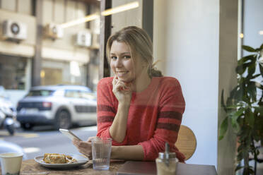 Glücklicher junger Freiberufler sitzt mit Smartphone im Café - JOSEF14742