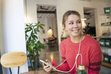 Glücklicher junger Freiberufler mit Smartphone in einem Café sitzend - JOSEF14749
