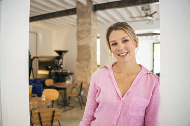 Glückliche blonde Geschäftsfrau, die sich in einem Café an die Wand lehnt - JOSEF14754