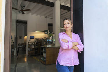 Thoughtful businesswoman with arms crossed standing in doorway at cafe - JOSEF14755