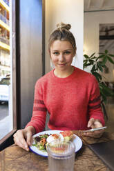 Smiling freelancer sitting with plate of food at table in cafe - JOSEF14772