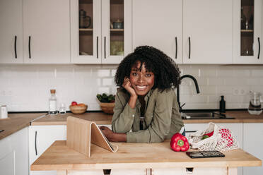 Smiling woman leaning by tablet PC on kitchen island at home - EBBF06942