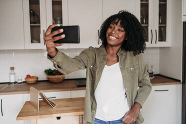 Lächelnde Frau nimmt Selfie durch Smartphone in der Küche zu Hause - EBBF06949