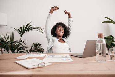 Happy businesswoman with arms raised at desk in home office - EBBF06962