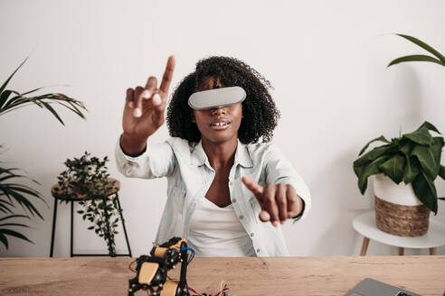 Junger Ingenieur trägt ein Virtual-Reality-Headset und gestikuliert im Büro zu Hause - EBBF06982