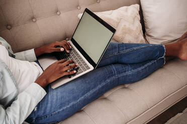 Businesswoman sitting on sofa using laptop at home - EBBF06993