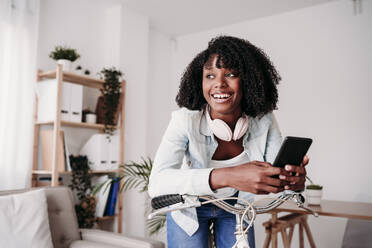 Happy woman with smart phone leaning on bicycle at home - EBBF07007