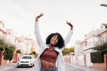 Carefree woman with arms crossed dancing on road - EBBF07010