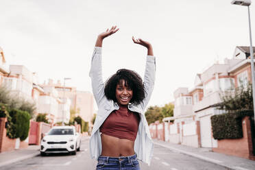 Young woman dancing on road with arms raised - EBBF07011