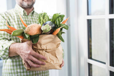 Älterer Mann hält Papiertüte mit frischem Gemüse vor der Tür - KMKF01884