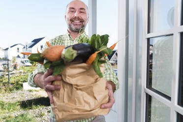 Ein lächelnder Mann mit einer Tasche voller frischem Gemüse steht an der Tür - KMKF01887