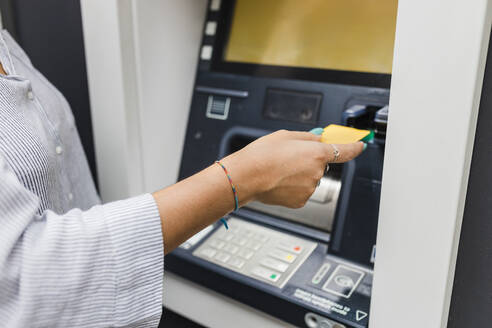 Hand einer Frau, die eine Kreditkarte in einen Geldautomaten einführt - JRVF03258