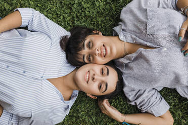 Lesbian couple lying with cheek to cheek on grass - JRVF03272