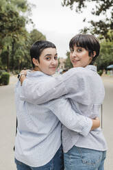 Lesbian women with arms around looking over shoulder at park - JRVF03279