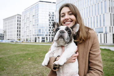 Glückliche Frau mit französischer Bulldogge vor einem Gebäude - EYAF02365