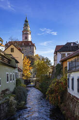 Tschechische Republik, Südböhmische Region, Cesky Krumlov, Fluss, der zwischen alten Stadthäusern fließt, mit dem Turm des Schlosses Cesky Krumlov im Hintergrund - WWF06253