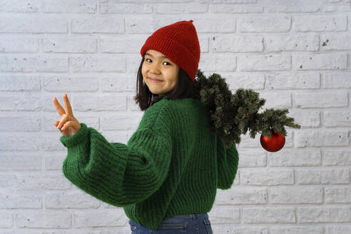 Lächelndes Mädchen mit Weihnachtsbaum gestikuliert Friedenszeichen - IEF00208