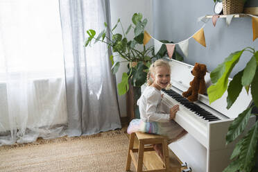 Glückliches Mädchen sitzt auf einem Hocker am Klavier zu Hause - SVKF00689