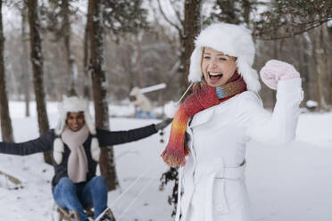 Happy woman flexing muscles with man sitting on sled in snow - OSF01119