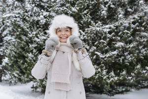 Cheerful woman wearing fur hat standing in front of tree - OSF01122