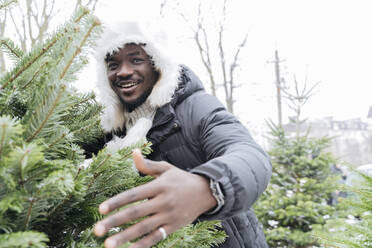 Fröhlicher Mann am Weihnachtsbaum auf dem Straßenmarkt - OSF01124