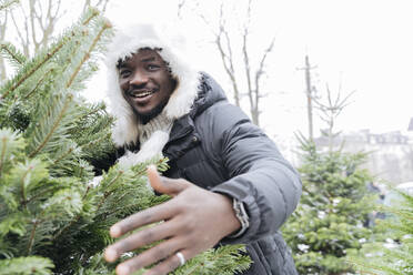 Happy man standing by Christmas tree at street market - OSF01124