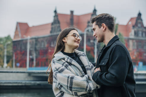 Lächelndes junges Paar sieht sich in der Nähe eines Geländers in der Stadt an - VSNF00105