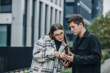 Young man and woman talking over mobile phone on street - VSNF00109