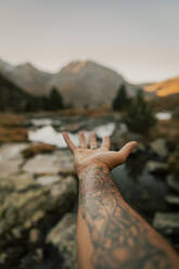 Man with tattooed hand gesturing towards lake - ACPF01526