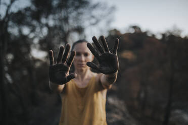 Frau mit ascheschwarzen Händen in einem verbrannten Wald stehend - DMGF00900