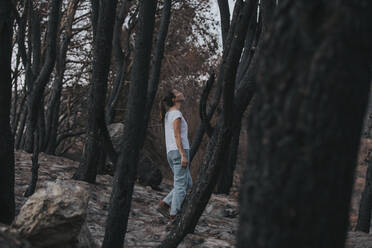 Frau geht inmitten verbrannter Bäume im Wald spazieren - DMGF00907