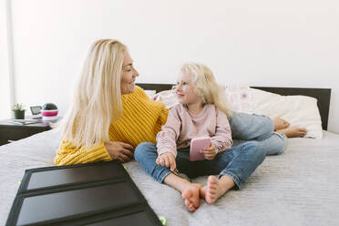 Happy mother and daughter sitting on bed at home - SIF00534