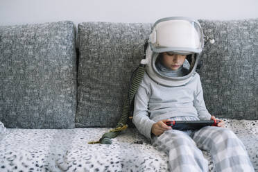 Niedliches Kind mit echter Astronautenuniform, das zu Hause auf der Couch sitzt und mit einer Videospielkonsole spielt - ADSF40308