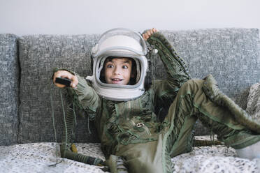 Niedliches Kind in einer echten Astronautenuniform, das fernsieht und eine Fernbedienung benutzt - ADSF40316